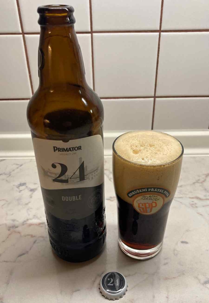 Nalité pivo Primátor 24 ve sklenici vedle láhve s hustou pěnou